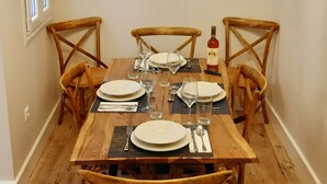 Comedor con mesa de madera dispuesta para cuatro personas, rodeada por cuatro sillas de mimbre.