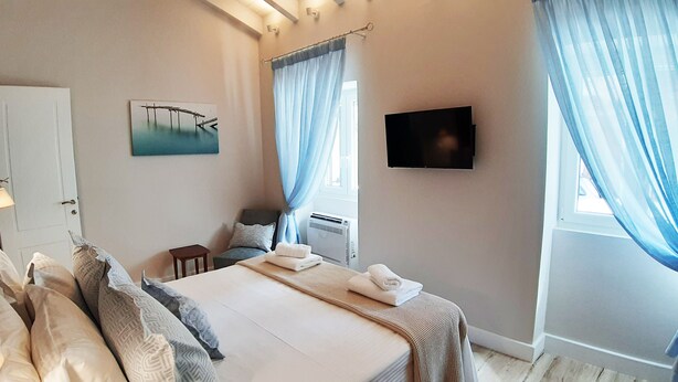 Un dormitorio con cama, televisión, ventana con cortinas, un cuadro y una puerta.