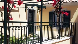 Un edificio con fachada color crema, contraventanas negras y barandilla metálica adornada con flores rojas.