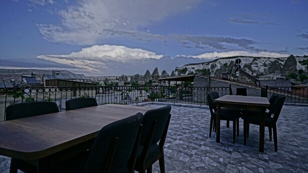 An outdoor seating area with tables and chairs, overlooking a mountainous landscape with a clear sky. - Epoch Stone House (Nevsehir)