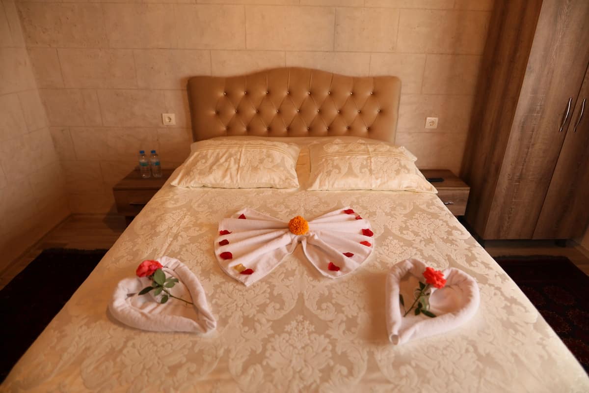A hotel room with a tufted headboard, two pillows, a neatly made bed with a decorative bow and rose-shaped towels.