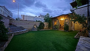 A well-maintained backyard with a lawn, a stone water feature, and a building with an entrance. - Epoch Stone House (Nevsehir)
