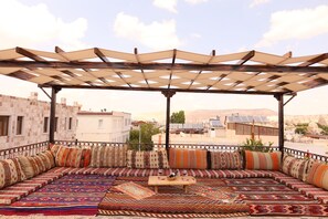 A covered outdoor seating area with patterned cushions and a table, overlooking a cityscape. - Epoch Stone House (Nevsehir)