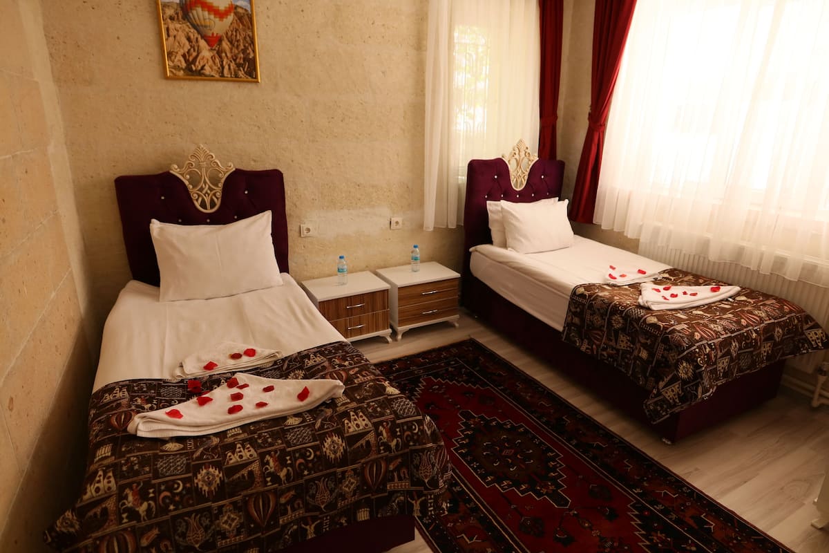 A hotel room with two beds, a nightstand, and a red patterned rug.