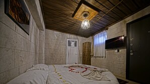 A bedroom with a bed, a wooden ceiling, a television, and a door. - Epoch Stone House (Nevsehir)