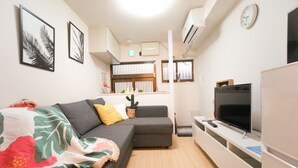 A living room with a grey sofa, a flat-screen TV, and a potted plant.