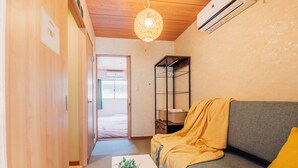En hall med trägolv, en soffa med ett gult överkast, en hängande lampa och en väggmonterad luftkonditioneringsanläggning.