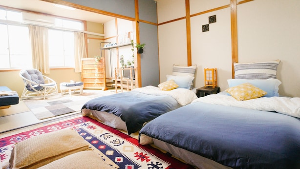 A hotel room with two beds, a sitting area with a chair and table, and a view of the outside. - TSURUYA (Osaka)