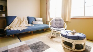 A cozy living room with a blue sofa, a white rocking chair, and a small ottoman. - TSURUYA (Osaka)