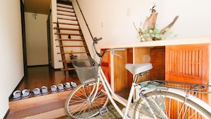 A bicycle parked next to a wooden cabinet with a basket, a wooden staircase, and a row of shoes on the floor. - TSURUYA (Osaka)