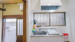 A compact kitchen with a sink, a window with blinds, a white stove, and a ceiling-mounted air conditioner. - NICE HOUSE (Osaka)