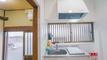 A compact kitchen with a sink, a window with blinds, a white stove, and a ceiling-mounted air conditioner.