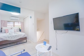 A bedroom with a bed, a small table with a remote control, and a TV mounted on the wall. - NICE HOUSE (Osaka)