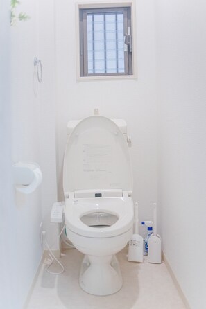 A small, white bathroom with a toilet, a window above the toilet, and a hand dryer to the right. - NICE HOUSE (Osaka)