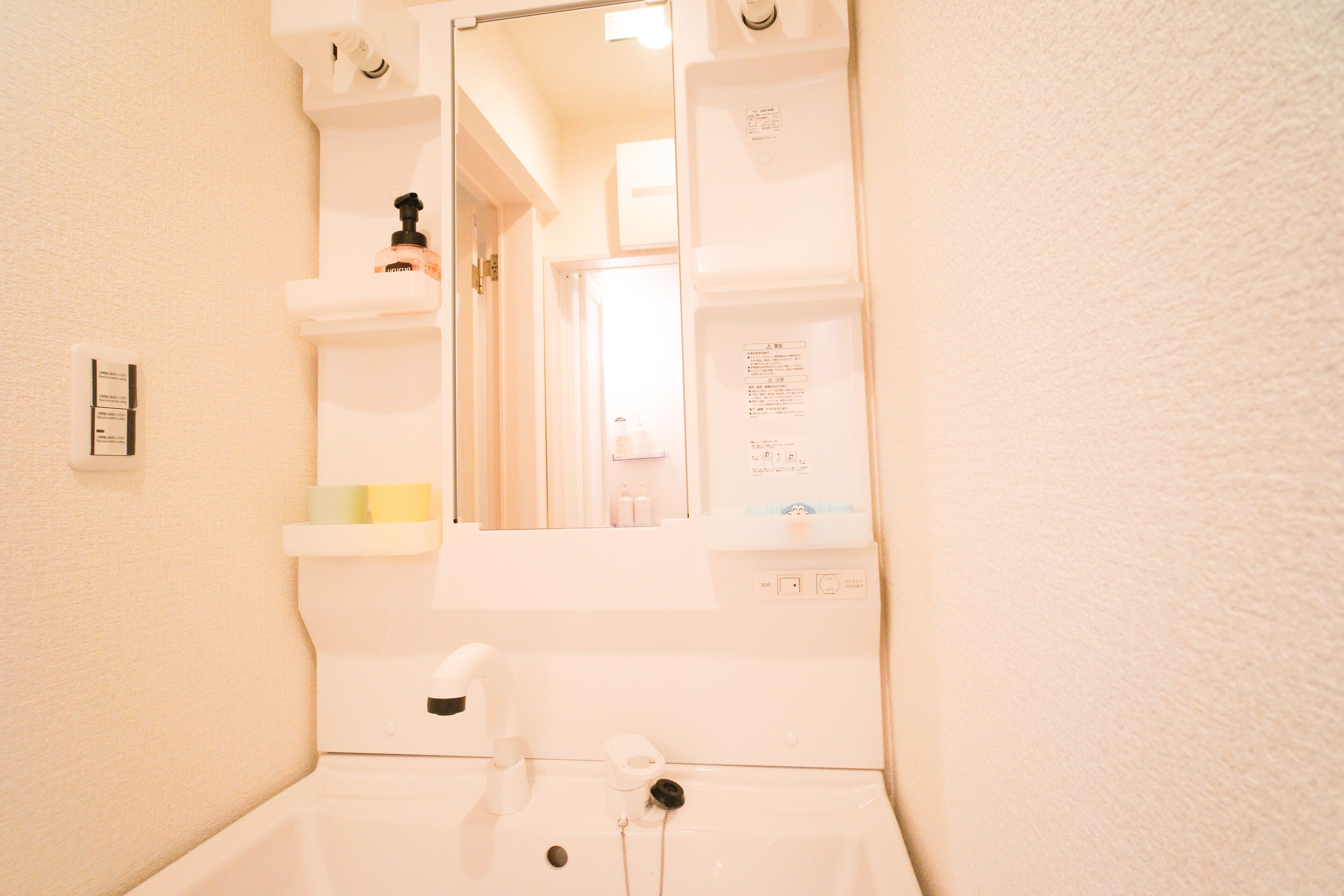 Un bagno con un lavandino bianco, uno specchio e uno scaffale con articoli da toilette.