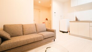A modern living room with a sofa, a small coffee table, and a kitchen area with cabinets and a refrigerator. - Doraemon's House (Osaka)