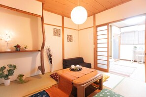 A traditional Japanese room with tatami flooring, a low table with a tray of tea, a sofa, and sliding doors leading to another room. - Tsurumibashi House (Osaka)