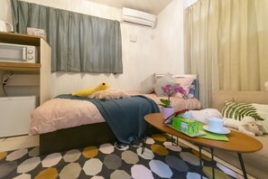 A cozy bedroom with a bed, a bedside table with a cup and box, a microwave, and a small heater. - MARE HOUSE-1F (Tokyo)
