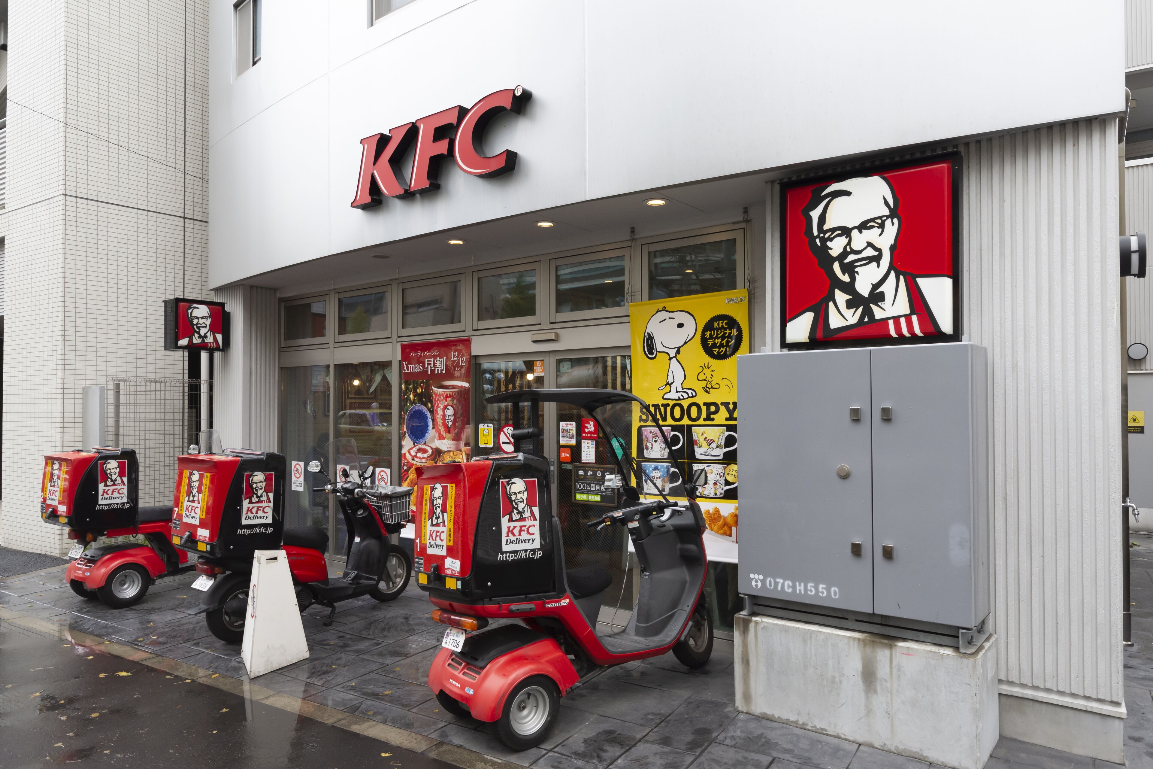 A KFC restaurant with a large sign, a delivery scooter, and a billboard featuring a cartoon character.