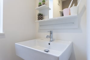 Ein weißes Waschbecken mit chromfarbenem Wasserhahn, ein Spiegel darüber und zwei Ablagen mit Pflanzen und Tassen.