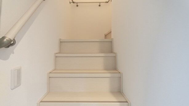 Un escalier en bois, avec une main courante sur le côté gauche et un interrupteur sur le mur.