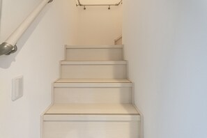 Un conjunto de escaleras de madera con barandilla a la izquierda y un interruptor de luz en la pared.