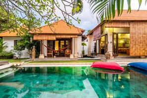 A swimming pool with a tiled deck, a hammock, and a building with a tiled roof and a glass door. - Madu Seminyak (Seminyak)