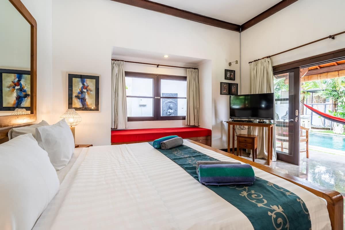 A hotel room with a large bed, a TV, a desk, and a view of a pool.