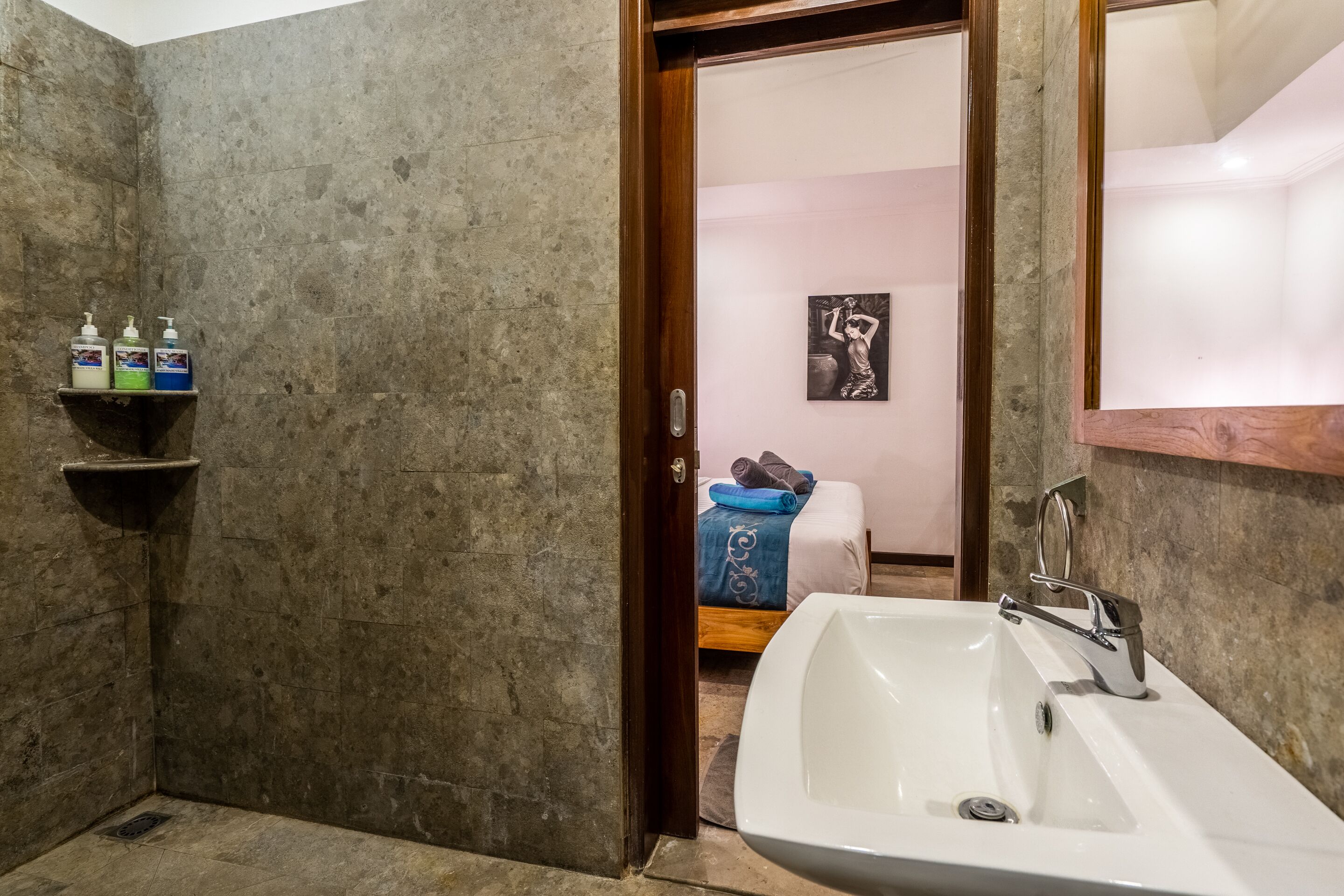 A bathroom with a white sink, a shower area, and a shelf with toiletries.