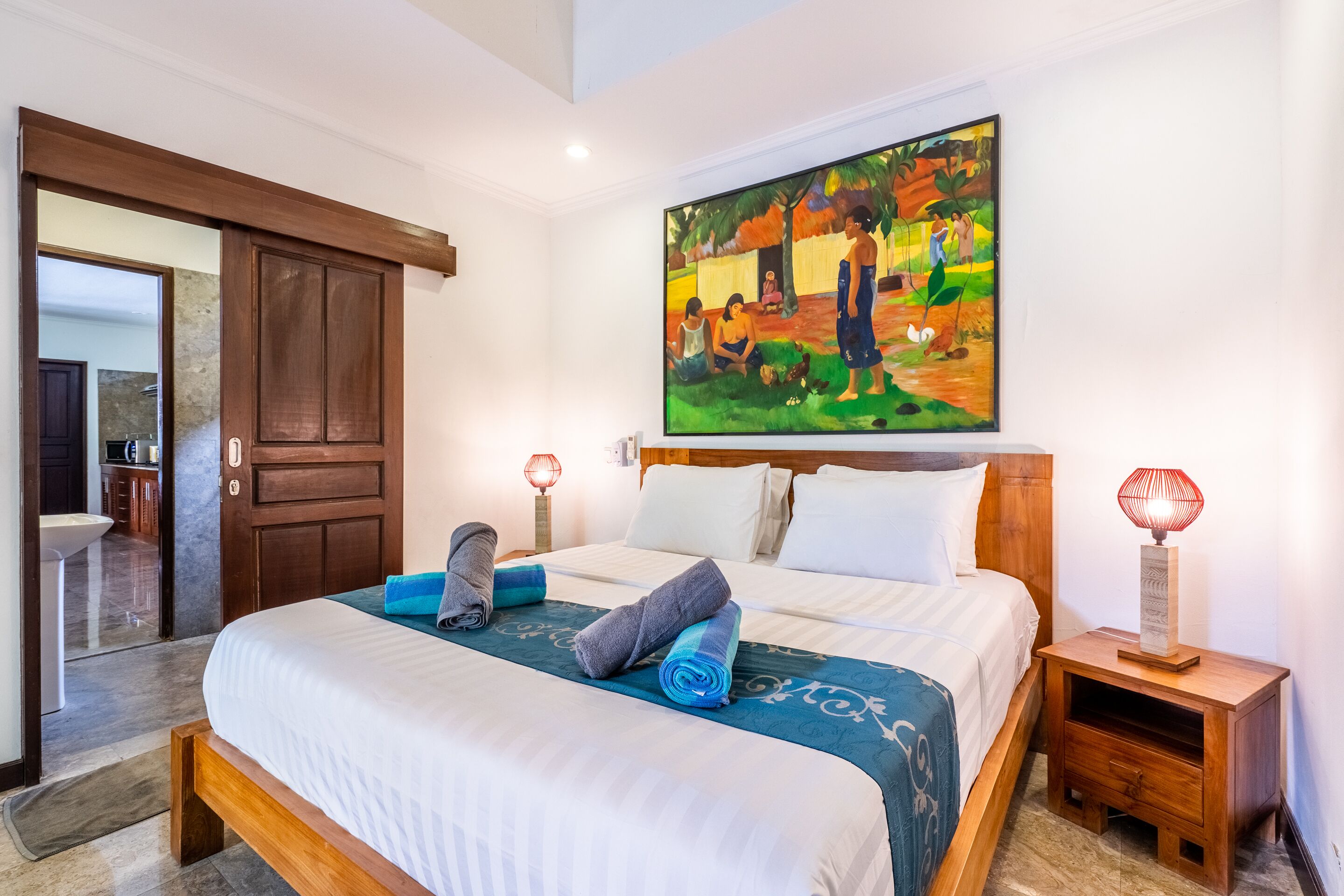 Une chambre d’hôtel avec un grand lit, une tête de lit en bois, un tableau au mur et une table de chevet avec une lampe.