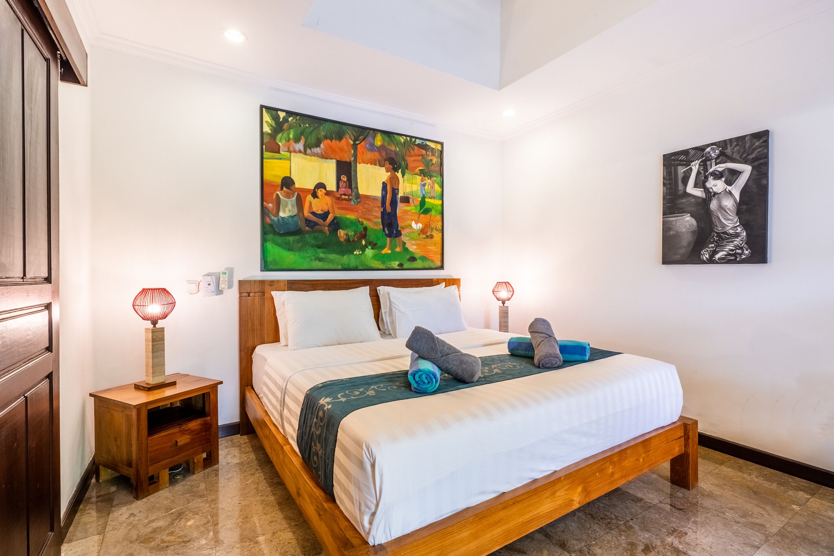 A bedroom with a wooden bed, white bedding, two bedside tables with lamps, and two paintings on the walls.
