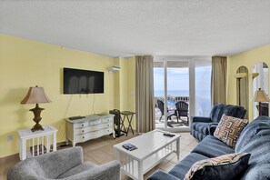 A living room with a sofa, armchair, coffee table, and a flat-screen TV mounted on the wall. - Adorable Oceanfront Oceanfront Condo (North Topsail Beach)