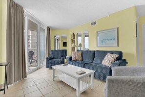 A living room with a sofa, armchairs, a coffee table, and a sliding glass door leading to an outdoor area. - Adorable Oceanfront Oceanfront Condo (North Topsail Beach)