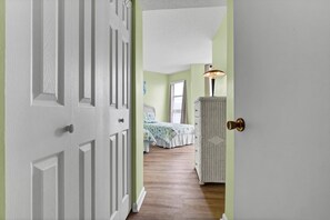 A hallway leading to a bedroom with a bed, a dresser, and a lamp.
