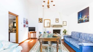 Uma sala de estar com sofá, televisão, lareira e lustre.