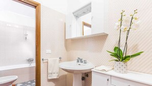 Casa de banho com lavatório branco, espelho e uma planta de orquídea.