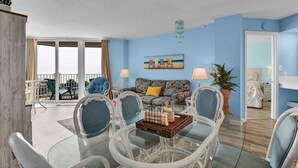 A living room with a sofa, chairs, a glass coffee table, and a painting on the wall. - Oceanfront condo with ocean views! (North Topsail Beach)