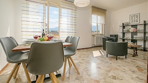 A dining area with a table set for four, chairs, a hanging light fixture, and a view through large windows. - Breath of Lake Garda Apartment (Riva del Garda)