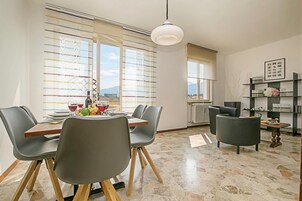 A dining area with a table set for four, chairs, a hanging light fixture, and a view through large windows.