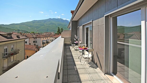 A balcony with a table and chairs, overlooking a town and mountains. - Breath of Lake Garda Apartment (Riva del Garda)