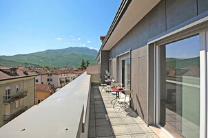 A balcony with a table and chairs, overlooking a town and mountains.