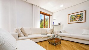 Un salon moderne avec un canapé d’angle, une table basse en verre et une grande fenêtre donnant sur des immeubles et des arbres.