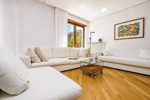 A modern living room with a sectional sofa, a glass coffee table, and a large window with a view of buildings and trees.