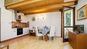 Une cuisine avec des meubles de rangement en bois, une table à manger avec des chaises, un téléviseur et un tableau accroché au mur.