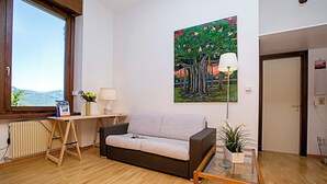 Un salon avec un canapé, une table, une lampe, un tableau et une vue par la fenêtre.