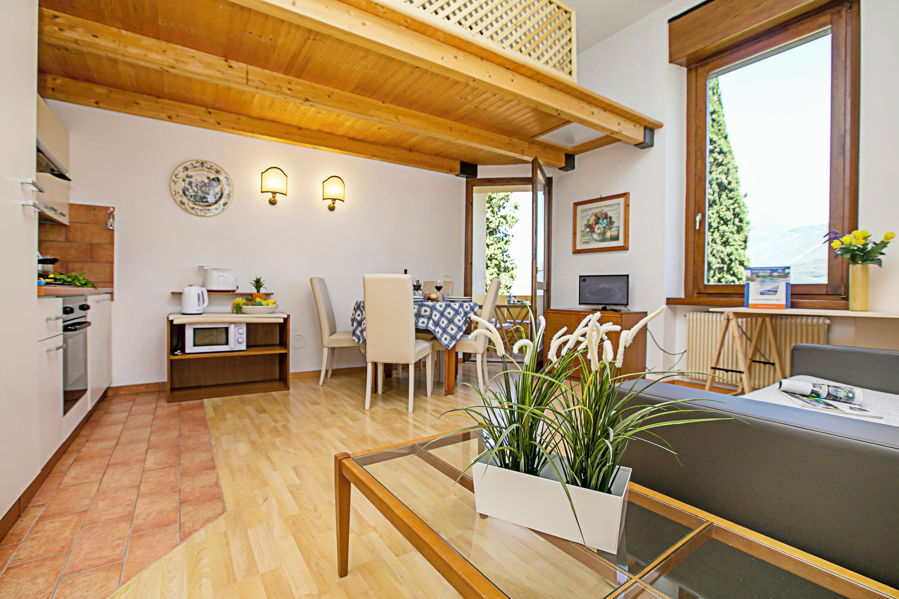 Una cucina moderna con travi in legno, un'area pranzo con tavolo e sedie, e un'ampia finestra con vista.