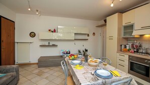 A dining area with a table set for two, a kitchen with modern appliances, and a living area with a sofa.