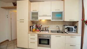 A compact kitchen with white cabinets, a stainless steel oven, a microwave, and a sink.