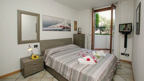 A bedroom with a bed, a nightstand, a lamp, a TV, and a window with curtains.