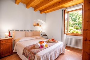A bedroom with a wooden ceiling, a bed with a white duvet, a bedside table with a lamp, and a window with a view of greenery. - Appartamento Centro Storico Riva (Riva del Garda)